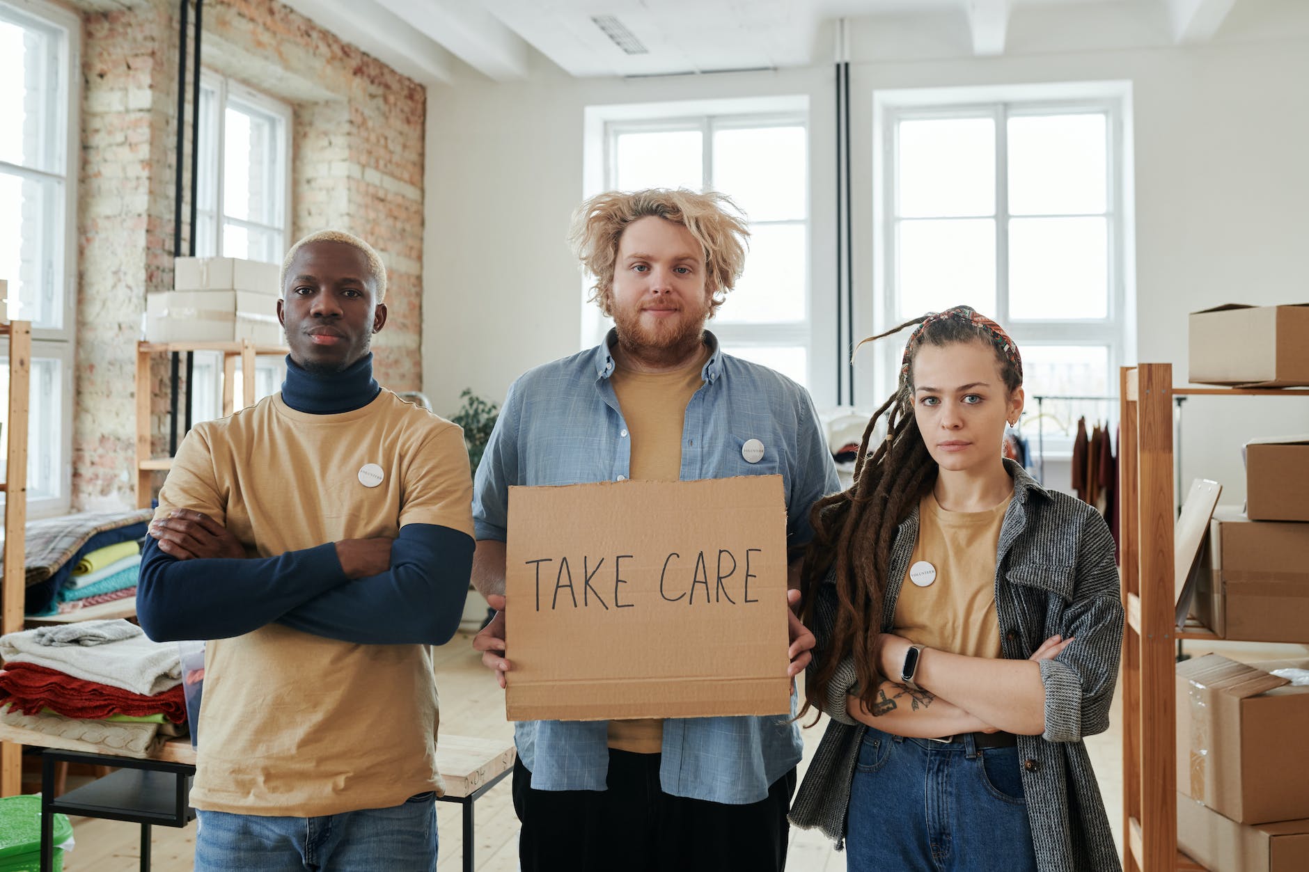 young men and woman standing holding a cardboard piece with take care written on it