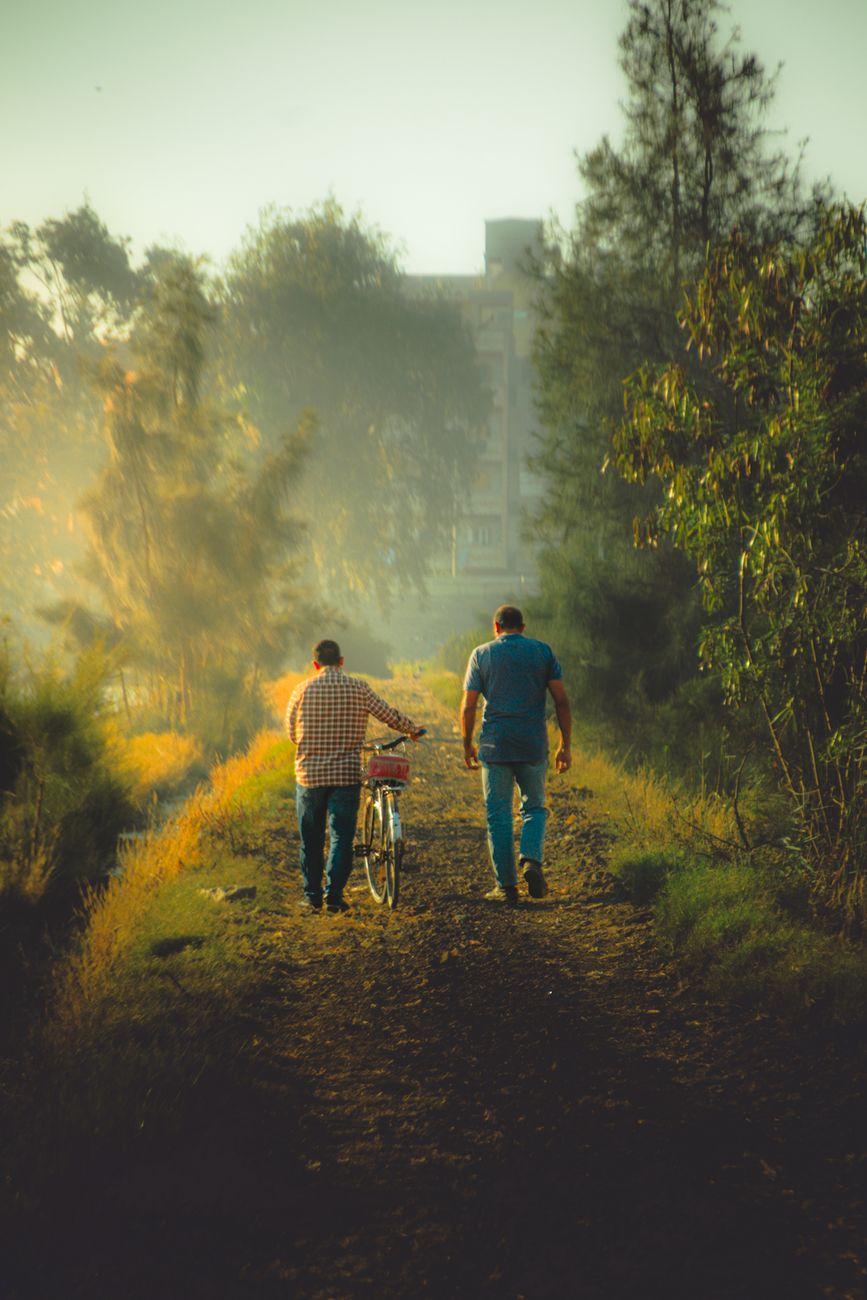 two men walking with bicycle on rural path at sunset